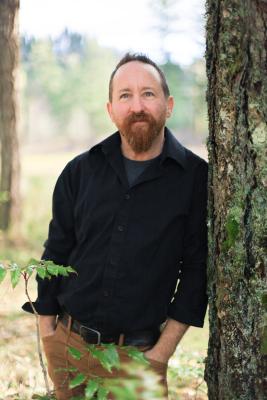 A photo of dean leaning against a tree with an approachable expression