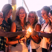 group of midlife women smiling together & holding sparkler